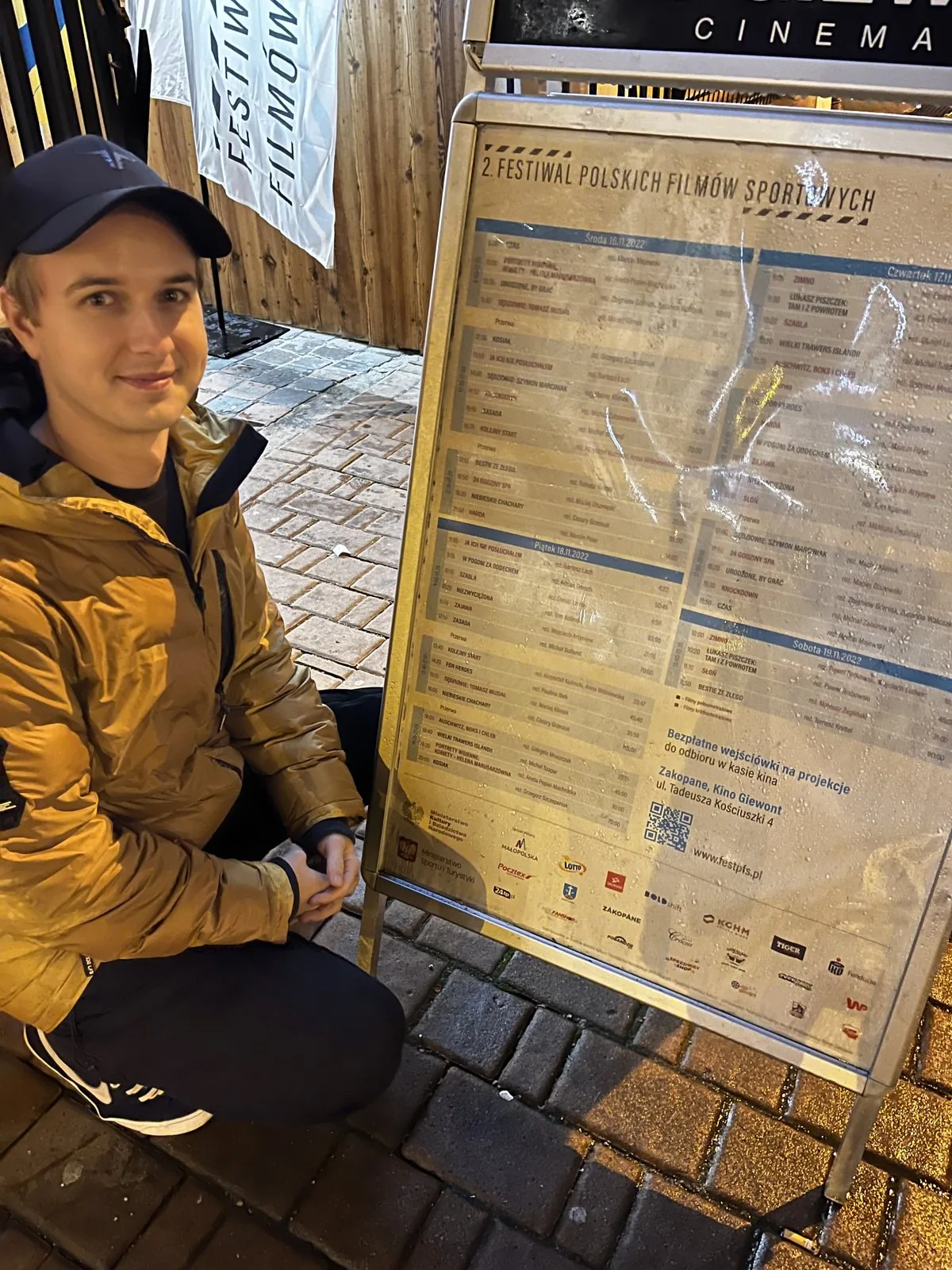 Maciek Olszewski przy tablicy z programem 2. Festiwalu Polskich Filmów Sportowych w Zakopanem, na której jest film 24 godziny Spa